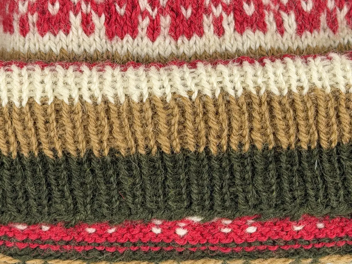 En stickad mössa, i mönsterstickad slätstickning, av 2-trådigt ullgarn. Mössan är rundstickad och har en fåll med 1-1 resår (1 rät och 1 avig maska) i nederkant, som är fastsydd med kaststygn. Toppen på mössan är formad med strålhoptagning och högst upp sitter en tofs fastsatt med en påtad snodd.
