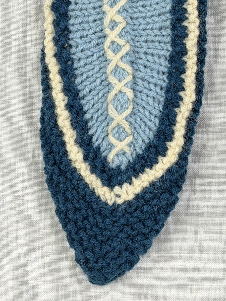 Två stickade tofflor, i slät- och rätstickning, av 3-trådigt ullgarn - Dubbelsport från Bergå Spinneri. Toffeln är hopsydd mitt fram med kaststygn och sedan dekorerad med korsstygn på rad, som ska likna en "snörning".
Gjord efter Bergå beskrivning innesockan Mysing från Bergå Färgeri & Ullspinneri, Stora Skedvi, Dalarna.