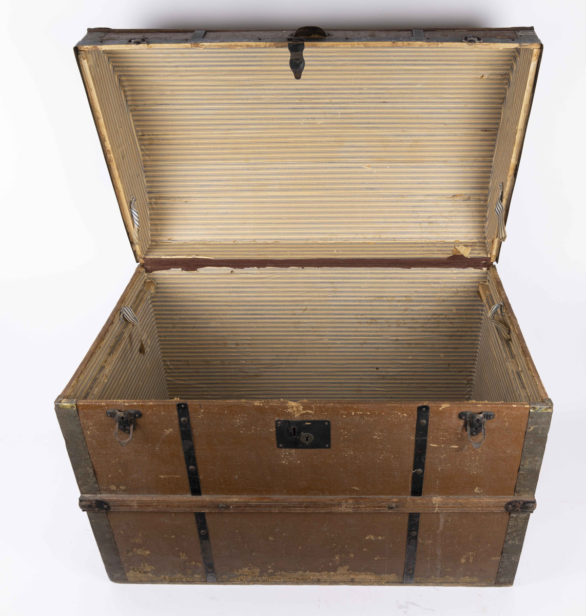 Stor amerikakoffert med buet lokk. Den er kledd med brunmalt lerret festet med trelister og svarte metallbeslag. Hver kortside har en metallhank, og fremsiden har tre metallåser. Innsiden er kledd med stripete papirtapet.