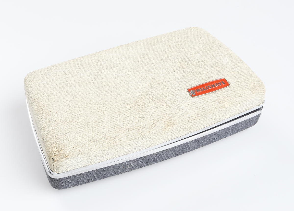 Elektrisk rakapparat tillverkad av plast i blått och vitt. Inuti det tvåfärgade plasthöljet finns en elektrisk motor som driver två roterande skär. Skären sitter i två runda, fjädrande skärhuvuden. På sidan av skärhuvudet finns luckor där avfallet tas ut. Anslutningskabeln är tillverkad av ljus plast eller syntetiskt gummi. Den har två ledare och en stickpropp i varje ände. Den ena stickproppen är avsedd att användas i både jordade och ojordade uttag. Den andra stickproppen sätts in i apparatens underdel. Rakapparaten förvaras i ett så kallat lyxetui, tillverkat av hårdplast i samma färger som rakapparaten. Inuti har den formgjuten inredning, klädd med rött sammetsliknanade tyg. Runt locket finns förkromade lister. Locket är fjäderbelastat. 
Tillverkad av Philips i Holland omkring 1960. Produktnamn Philishave Type SC 7860.