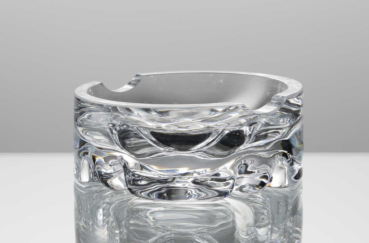 Askfat, rund form, tjockväggig med rutmönster i botten. Två nedsänkningar i kanten för cigaretter,
Formgivare: Olle Alberius.
