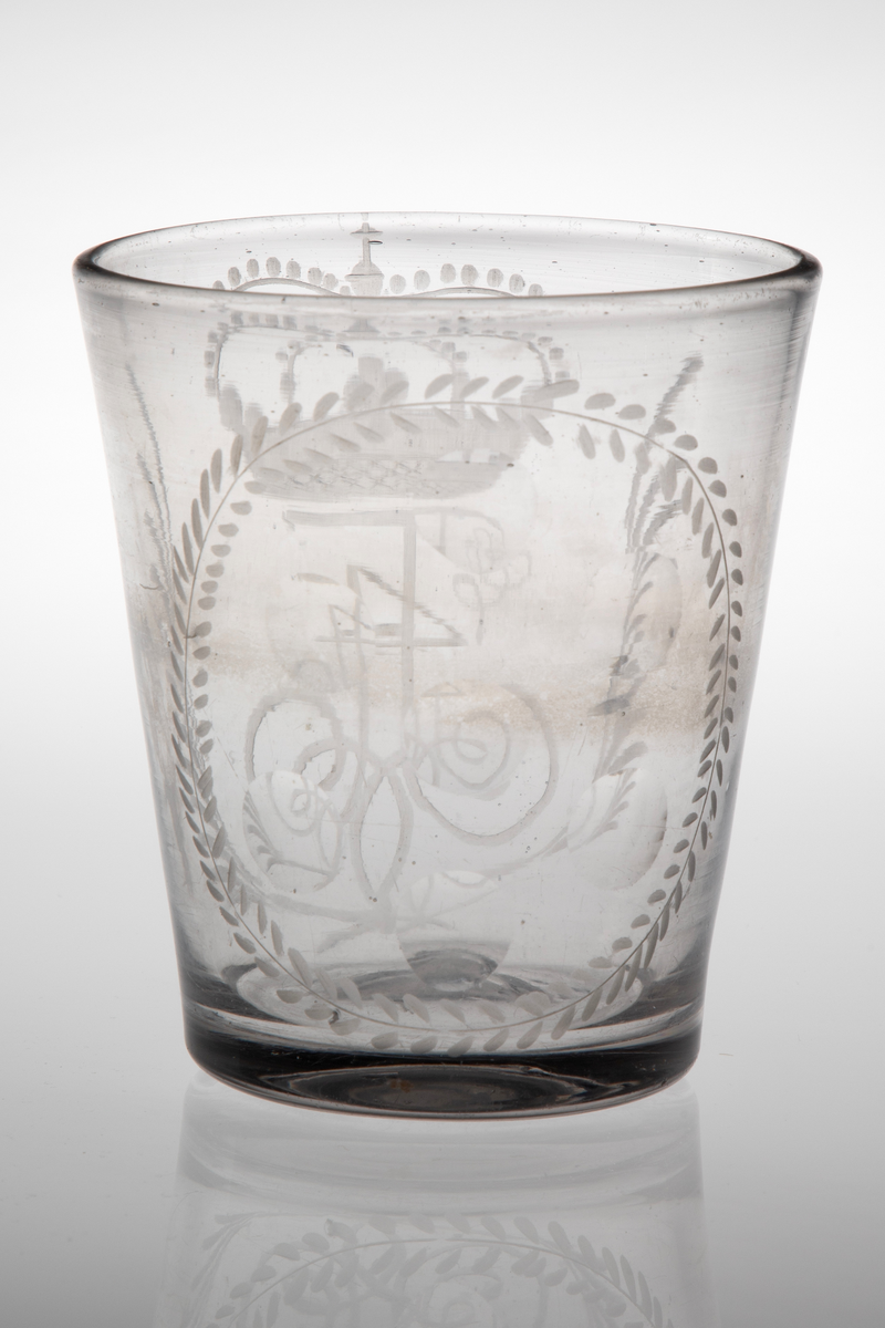 Beger i klart glass. Tilnærmet sylinderformet korpus med svakt koniske vegger i tykt glass. Yttersiden er dekorert med sliping og gravering. På den ene siden Fredrik IVs bekronede monogram, omgitt av to kryssende bladverk. På den andre siden en oval i form av en gravert stilisert plantebord som omkranser seks slipte sirkler. Rester etter puntemerke, noe grålig glassmasse.