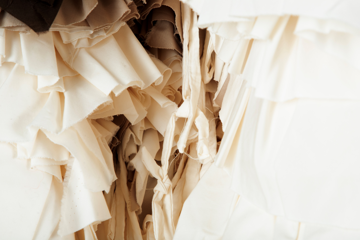 Tekstil skulptur i lyse farger som henger fra en frittstående firesidet ramme lagd av stenderverk i tre.