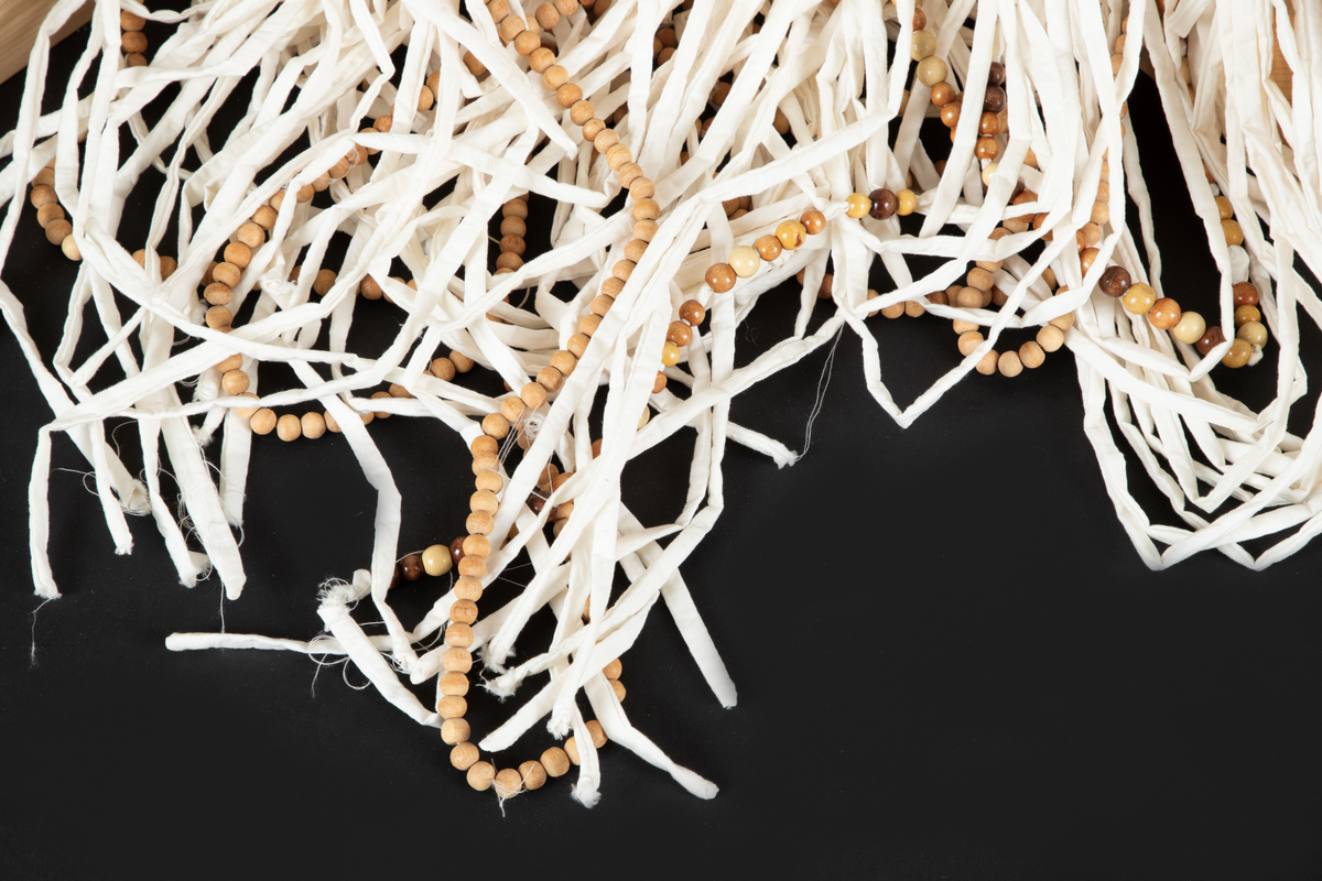 Tekstil skulptur i lyse farger som henger fra en frittstående firesidet ramme lagd av stenderverk i tre.