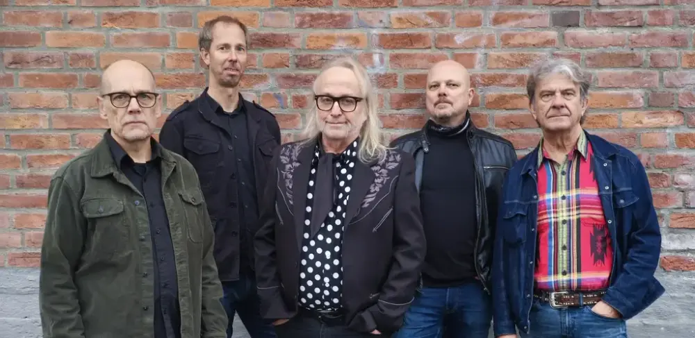 Fem menn poserer foran en murvegg. Det er Levi Henriksen og bandet Babylon Badlands.