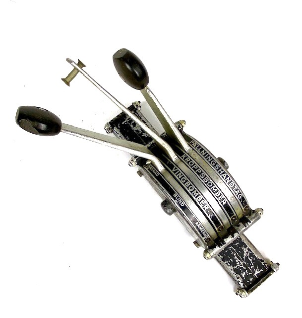 Bombväljare i metall, svartmålad. Tre spakar för val av fällningshandtag, kroppsbomber eller vingbomber -  säkrad, blind, armerad. Bakelitknopp på handtagen.