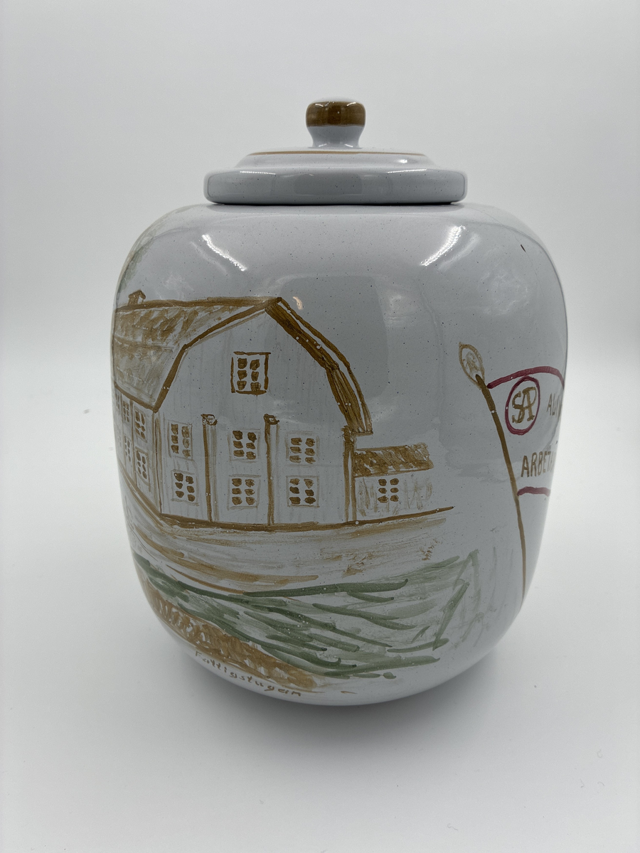 Urna med lock. Vitglaserad med handmålat motiv föreställande Alingsås fattigstuga, fana för Alingsås arbetarekommun och ålderdomshem.