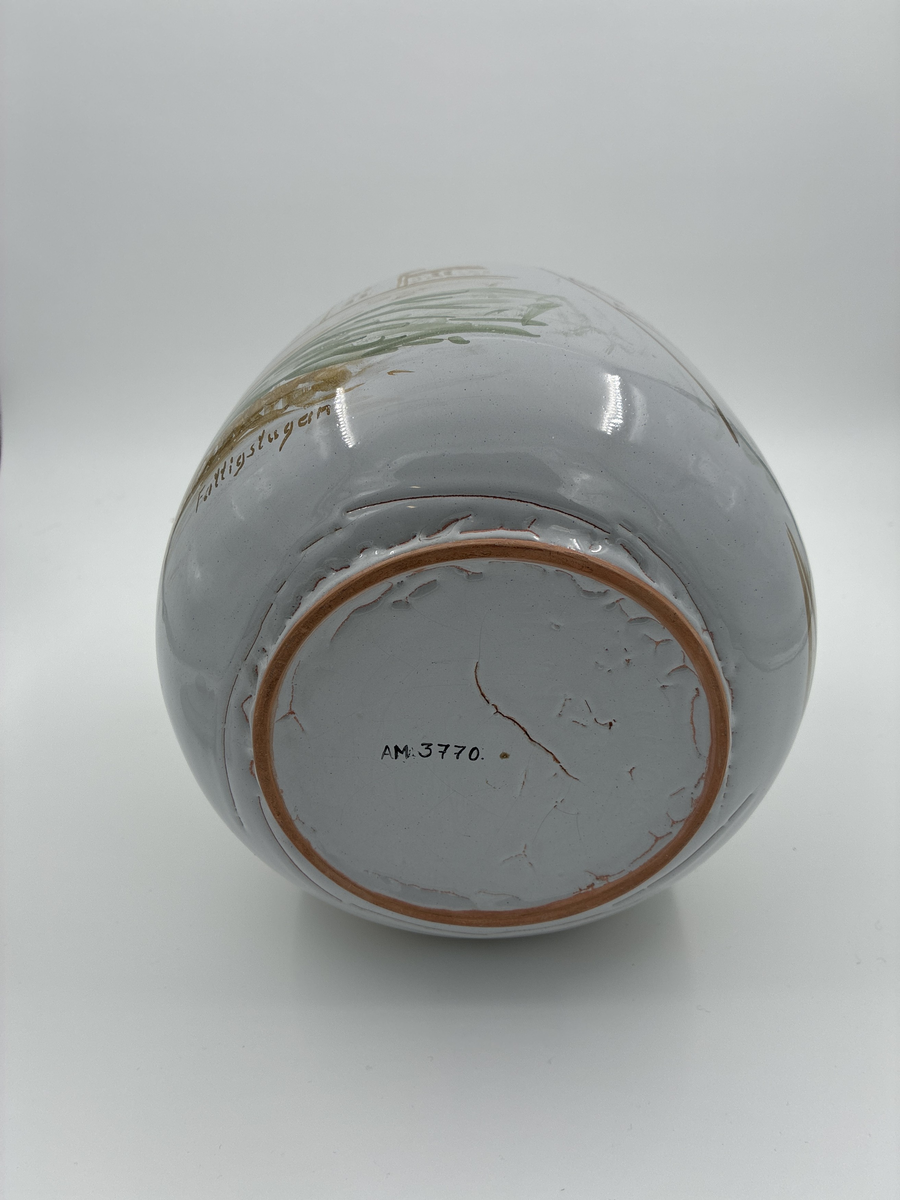 Urna med lock. Vitglaserad med handmålat motiv föreställande Alingsås fattigstuga, fana för Alingsås arbetarekommun och ålderdomshem.