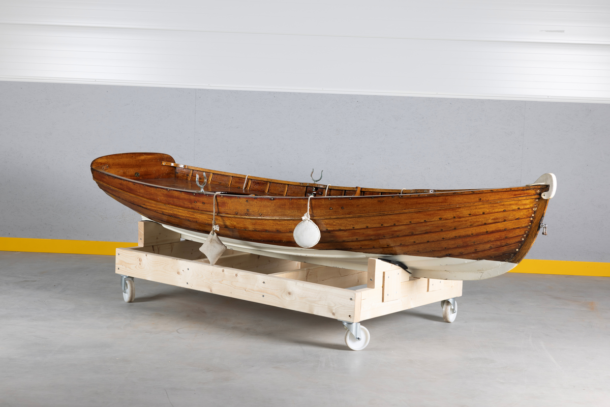 Kutterjolle med tiljer og to årer. Åregafler i metall og stoppede fendere i tekstil. Kjølen og nedre del av skroget er malt hvit.