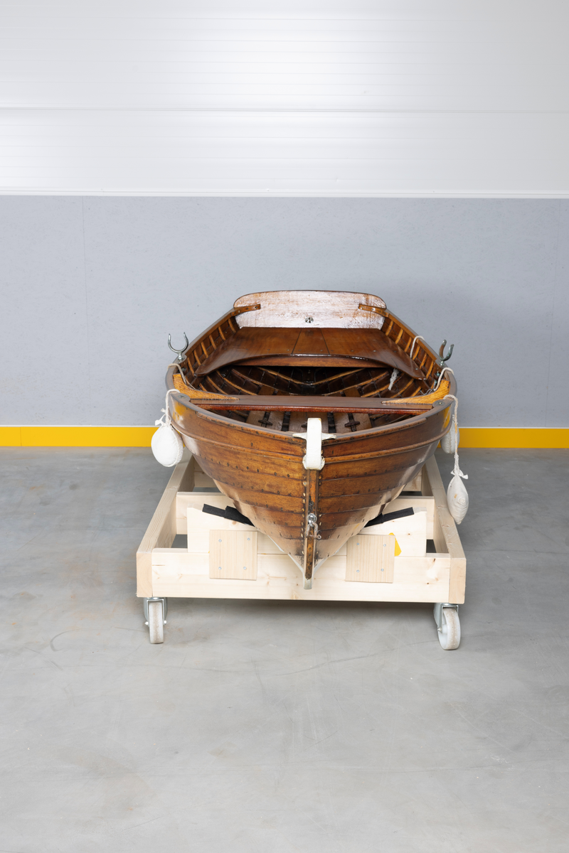 Kutterjolle med tiljer og to årer. Åregafler i metall og stoppede fendere i tekstil. Kjølen og nedre del av skroget er malt hvit.