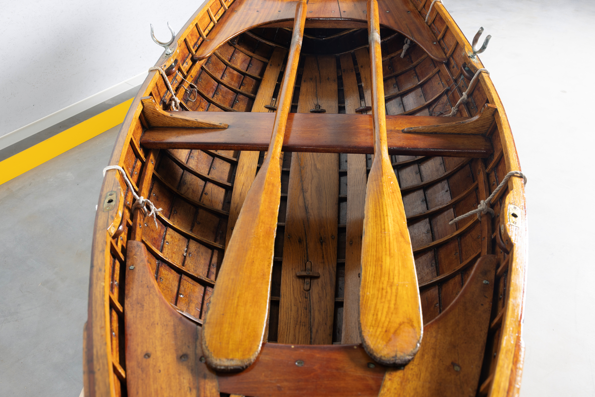 Kutterjolle med tiljer og to årer. Åregafler i metall og stoppede fendere i tekstil. Kjølen og nedre del av skroget er malt hvit.