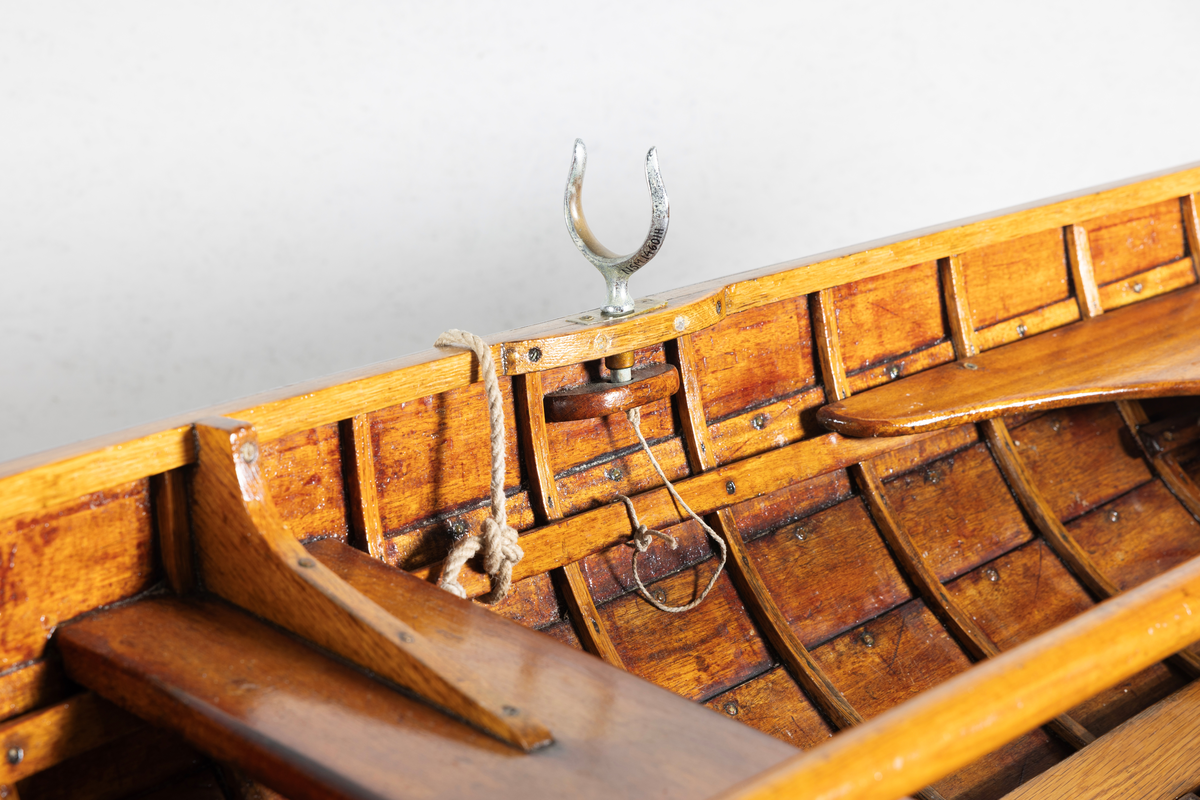 Kutterjolle med tiljer og to årer. Åregafler i metall og stoppede fendere i tekstil. Kjølen og nedre del av skroget er malt hvit.