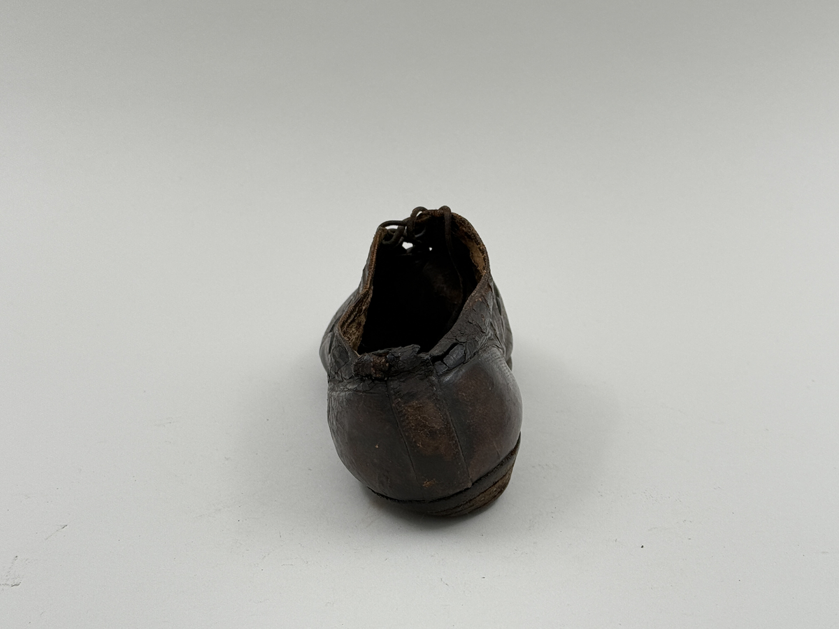 Damsko gjord på rak läst, spetsig lätt rundad tå. Lädret över tån skuret med dekorativt mönster av halvcirklar. Fem par snörhål, vissa med mässingsöljetter. Lädersula, liten klack. Lädret i hälen skadat.
 