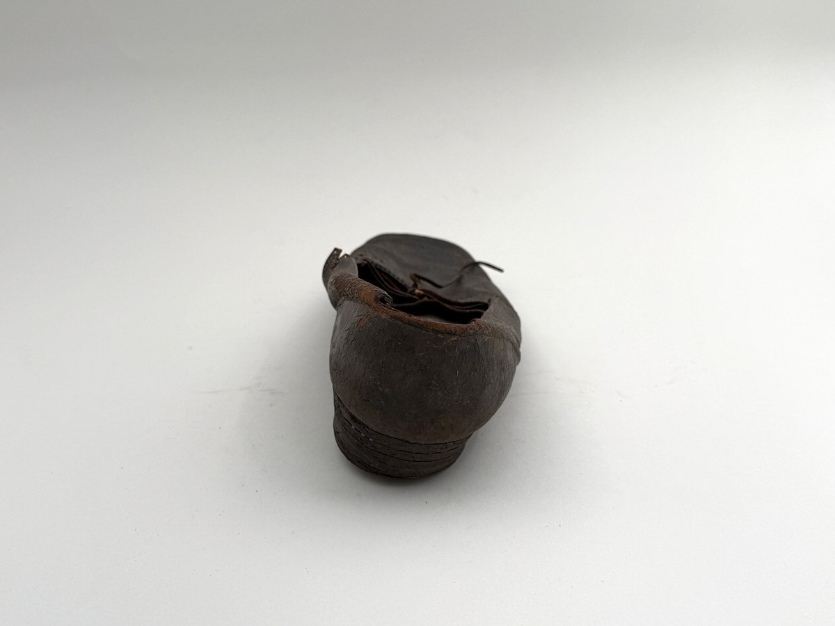 Sko för högerfot av svart läder, träpliggad sula av läder samt med becksömnad. Lädret löper över i två sleifer över plösen, genom plösen och sleifarna hål för snöre. Lädret skadat vid sleifarna. 