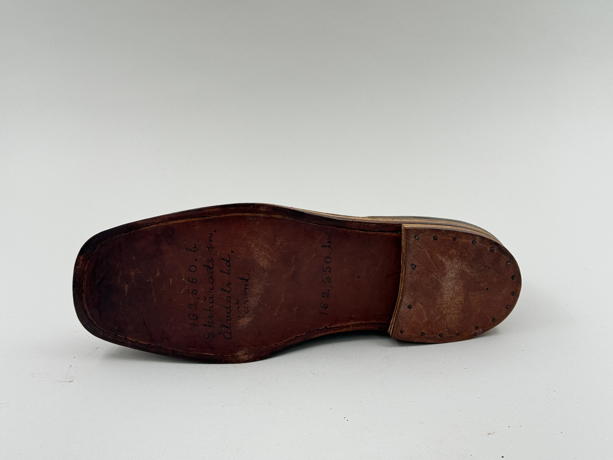 Låg snörkängor för vänster fot, av mörkbrunt läder med präglat stjärnmönster. Kanten upptill rakt avskuren. 4 par snörhål. Slitsula av läder med mellansula av näver, becksömmade. Innersula av näver. Klack järnpliggad. Nygjord efter gammal modell av givaren för museet.