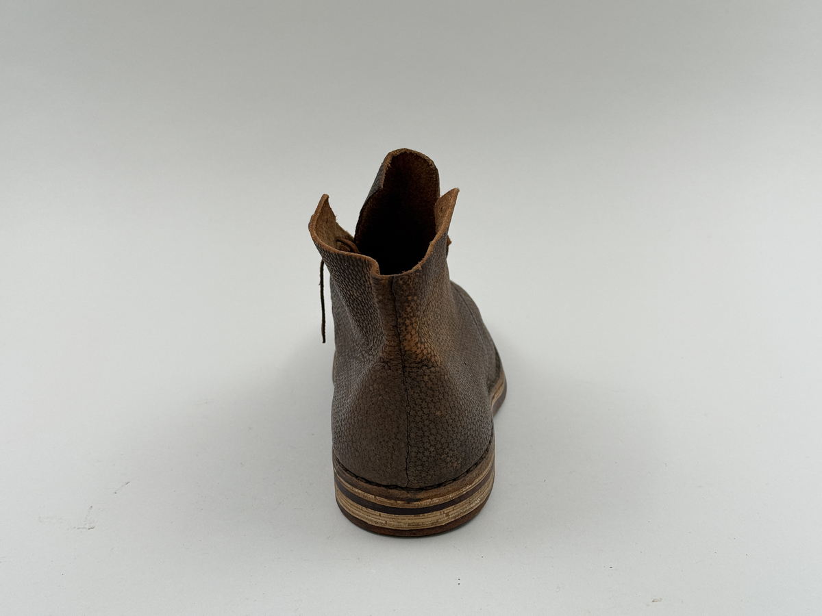 Låg snörkängor för höger fot,  av mörkbrunt läder med präglat stjärnmönster. Kanten upptill rakt avskuren. 4 par snörhål. Slitsula av läder med mellansula av näver, becksömmade. Innersula av näver. Klack järnpliggad. Nygjord efter gammal modell av givaren för museet.