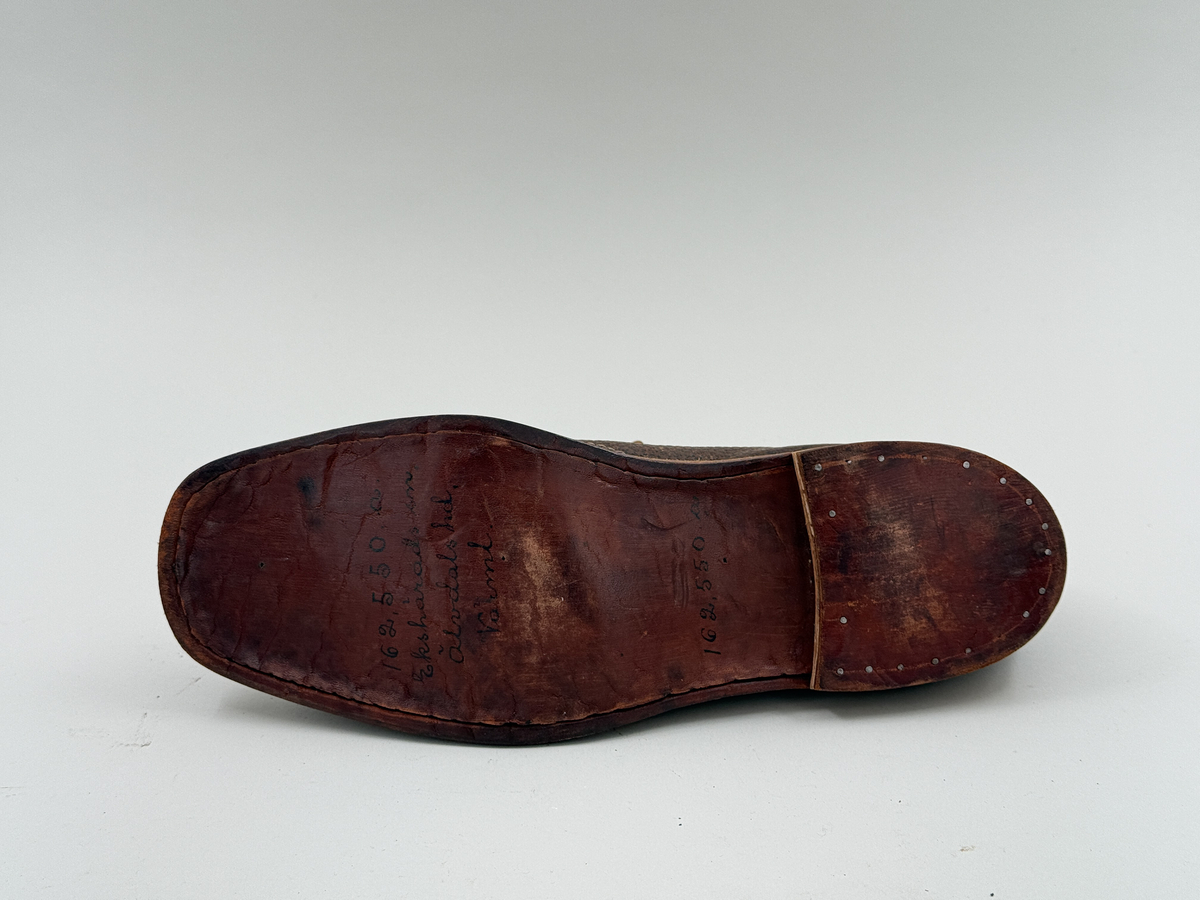 Låg snörkängor för höger fot,  av mörkbrunt läder med präglat stjärnmönster. Kanten upptill rakt avskuren. 4 par snörhål. Slitsula av läder med mellansula av näver, becksömmade. Innersula av näver. Klack järnpliggad. Nygjord efter gammal modell av givaren för museet.