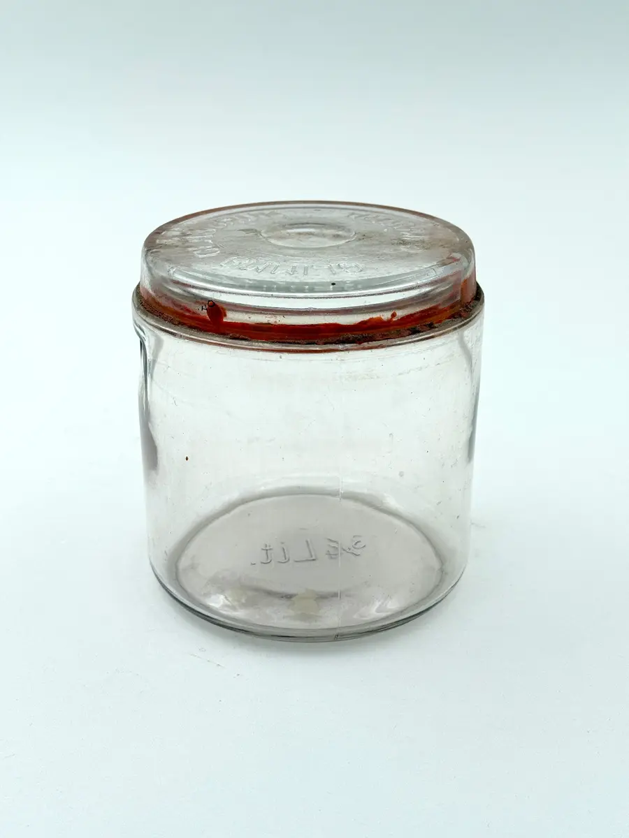 Cylindrisk burk av glas med lock och tätningsring av gummi. Locket med firmanamn i relief: GLIMMA GLASBRUK GLIMÅKRA. Botten med volymangivelse i relief: 3/4 LIT. 

Metallbygel saknas. 