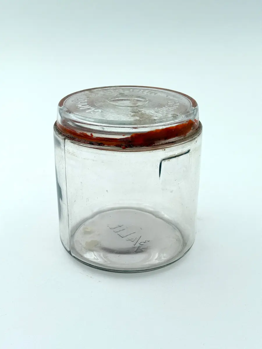 Cylindrisk burk av glas med lock och tätningsring av gummi. Locket med firmanamn i relief: GLIMMA GLASBRUK GLIMÅKRA. Botten med volymangivelse i relief: 3/4 LIT. 

Metallbygel saknas. 