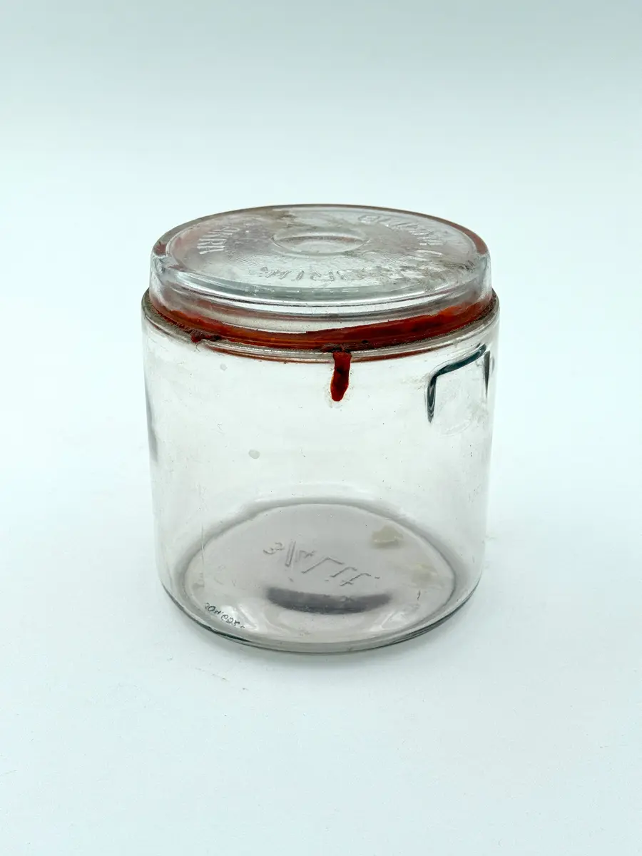 Cylindrisk burk av glas med lock och tätningsring av gummi. Locket med firmanamn i relief: GLIMMA GLASBRUK GLIMÅKRA. Botten med volymangivelse i relief: 3/4 LIT. 

Metallbygel saknas. 