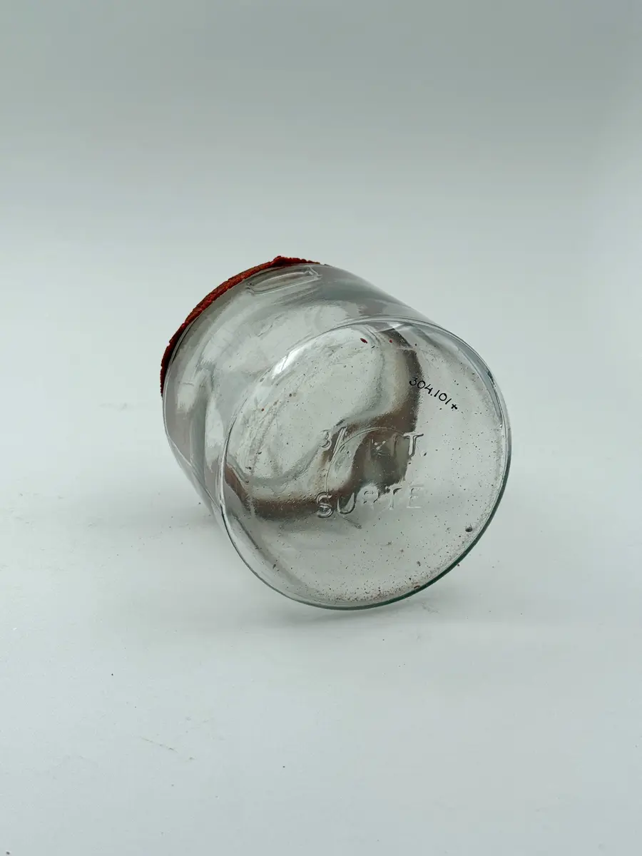 Cylindrisk burk av klarglas med lock och gummiring. Glaset formgjutet. Burken med intag i glaset på vardera sida för fästa av metallbygel som ska hålla locket på plats. Locket märkt GLIMMA GLASBRUK GLIMÅKRA, och botten märkt 3/4 LIT. SURTE. 

Metallbygel saknas. Locket sitter fast i den torkade gummiringen. 