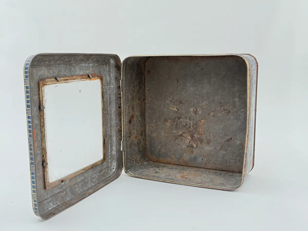 Kvadratisk burk av plåt med lock, locket med infällt glas. Tryckt dekor av vinrankor och vindruvor mot blå bakgrund, Smala röda bårder upptill och nedtill med texten MAZETTI.