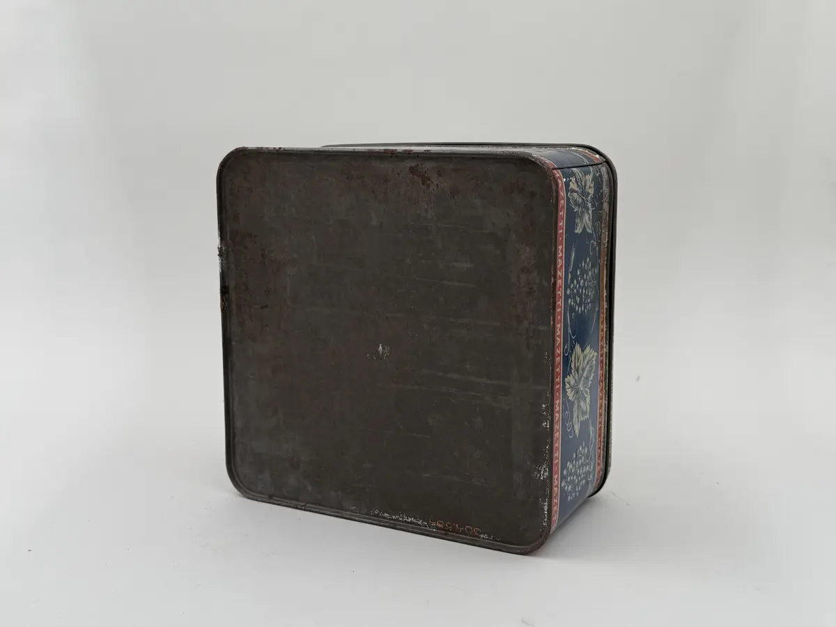 Kvadratisk burk av plåt med lock, locket med infällt glas. Tryckt dekor av vinrankor och vindruvor mot blå bakgrund, Smala röda bårder upptill och nedtill med texten MAZETTI.