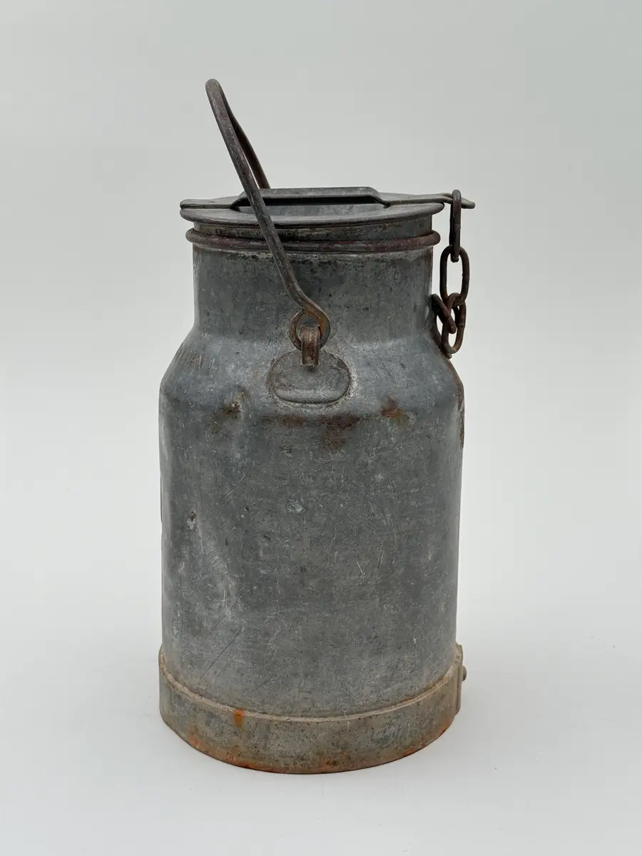 Cylindrisk mjölkflaska av plåt med något indragen hals. Platt lock samt uppsvängt handtag fäst i metallöglor på vardera sida. Märkt NÅDHAMMARBODARNA i låg relief samt med ett N med en hammare igenom i relief.

Locket fastkilat.