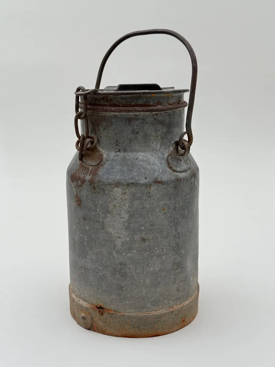 Cylindrisk mjölkflaska av plåt med något indragen hals. Platt lock samt uppsvängt handtag fäst i metallöglor på vardera sida. Märkt NÅDHAMMARBODARNA i låg relief samt med ett N med en hammare igenom i relief.

Locket fastkilat.
