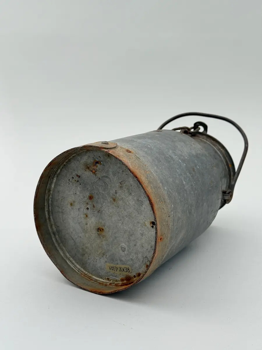 Cylindrisk mjölkflaska av plåt med något indragen hals. Platt lock samt uppsvängt handtag fäst i metallöglor på vardera sida. Märkt NÅDHAMMARBODARNA i låg relief samt med ett N med en hammare igenom i relief.

Locket fastkilat.