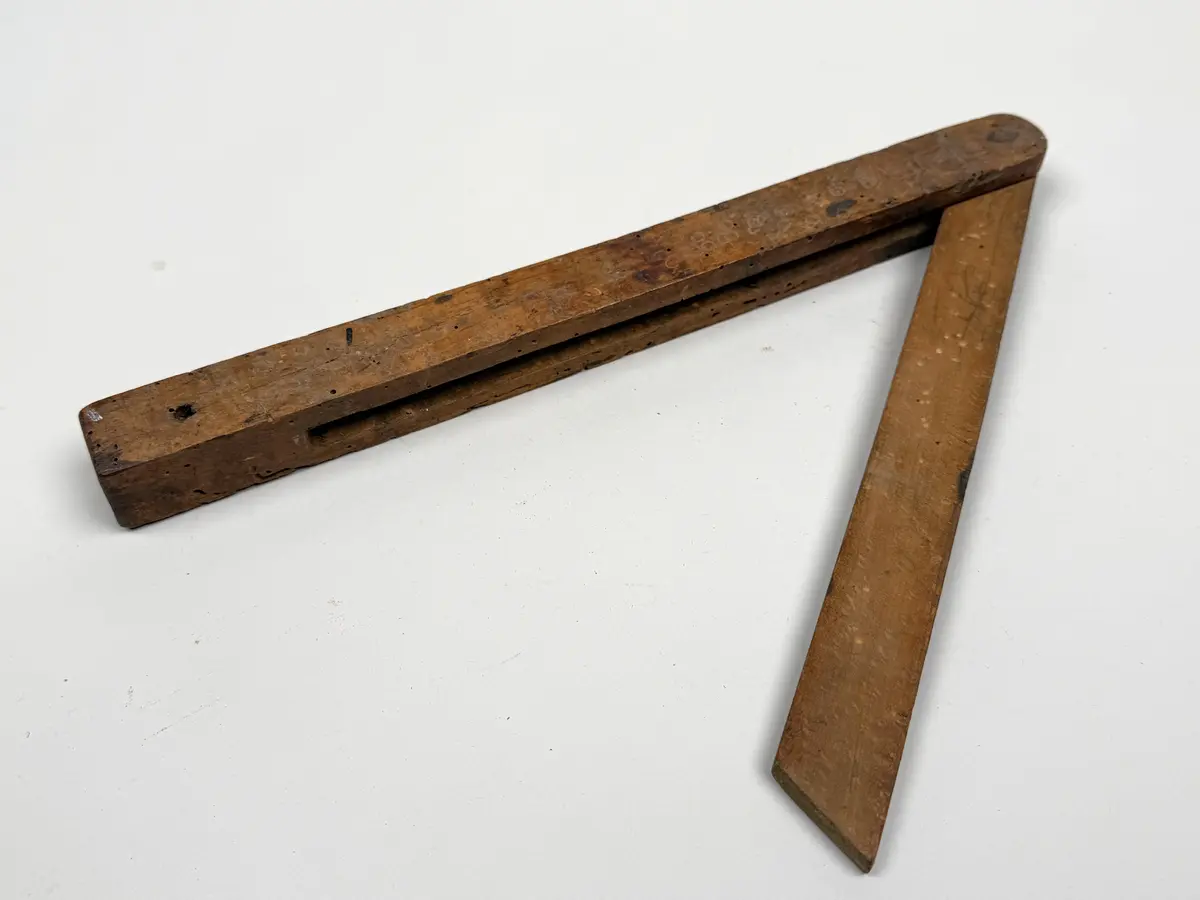 Utfällbart mått av trä. Anslag och utfällbart och ställbart blad fästa med metallskruv. Hål för upphängning. 

Maskstungen.