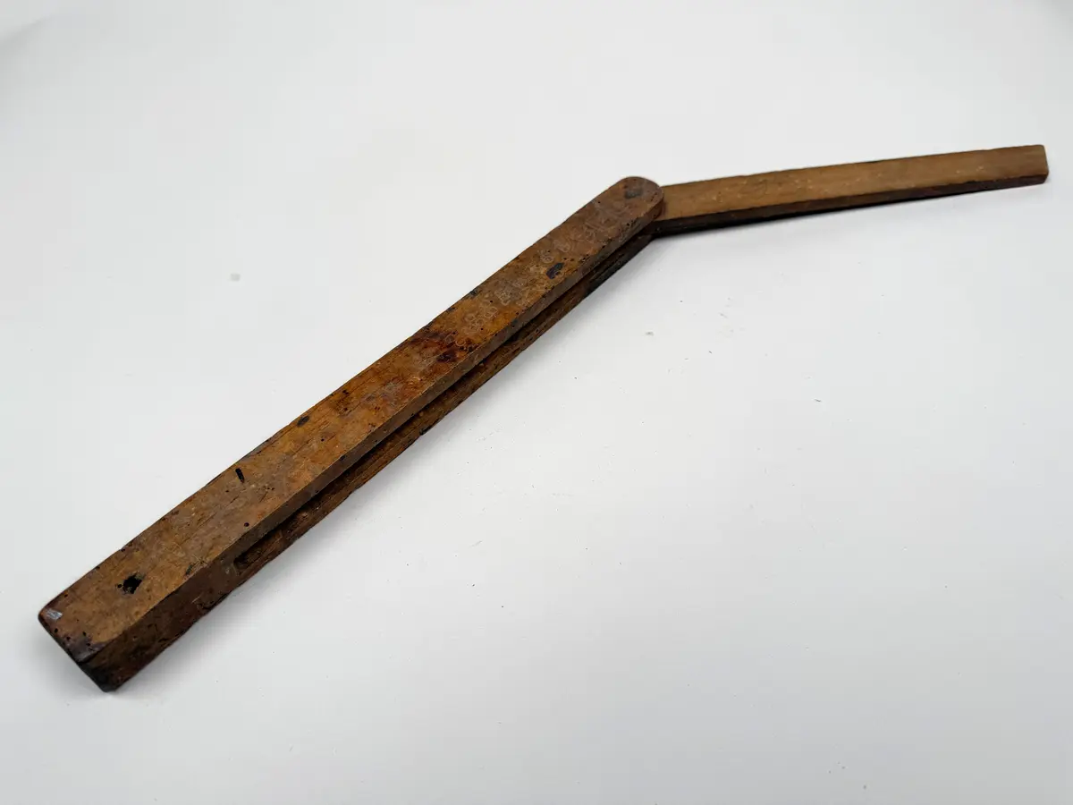 Utfällbart mått av trä. Anslag och utfällbart och ställbart blad fästa med metallskruv. Hål för upphängning. 

Maskstungen.