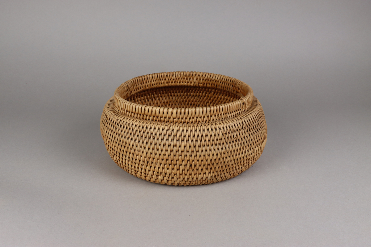 Korg bunden av kluvna rottågor över vidjor med löst lock. Rund bukig form med platt botten och platt lock.