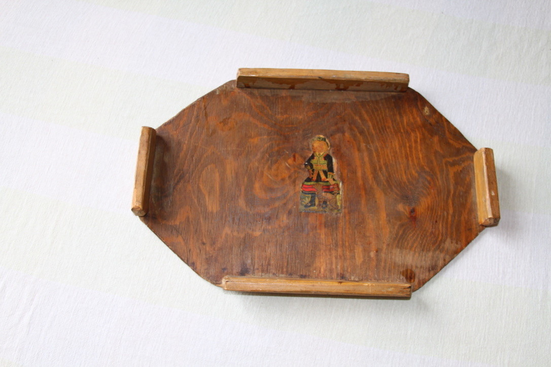 Åttekanta brunbeisa serveringsbrett i tre, gjenstanden er i god stand. Dekor i midten av brettet. Dekoren er ei dame i setesdalsbunad.