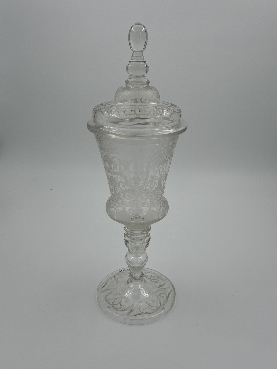 Pokal med lock. Av glas med riklig etsad dekor. 

Enligt säljarens uppgift har pokalen varit en gåva till fru von Proschwitz, Floda herrgård vid dennas 50-årsdag.
Efter hennes bortgång överlämnades pokalen som minnesgåva till dr G. Nystedt för dennas mångåriga tjänst som husläkare hos familjen Proschwitz.