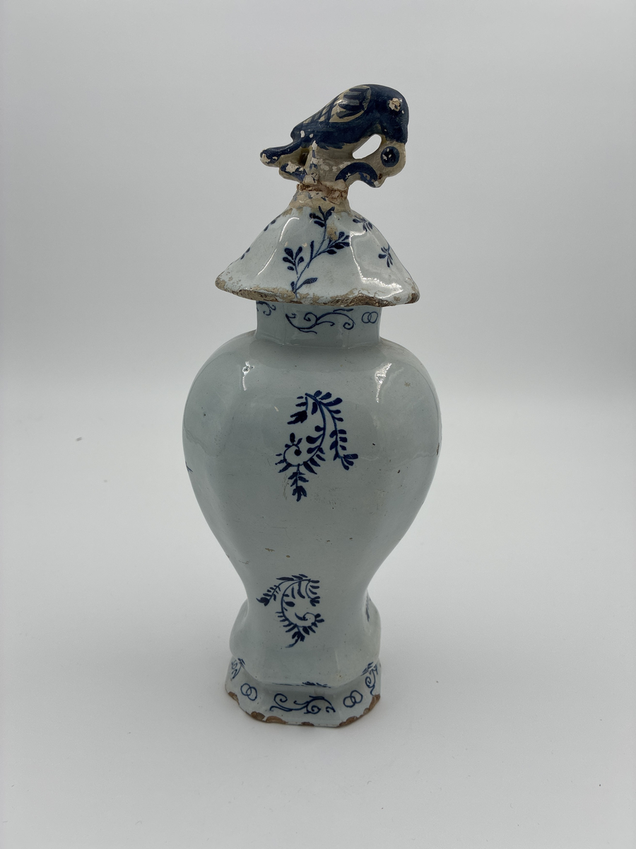 Urna med lock. Av glaserad fajans med dekor i blått. Locket dekorerad med fågel, defekt. Troligen från Delft.