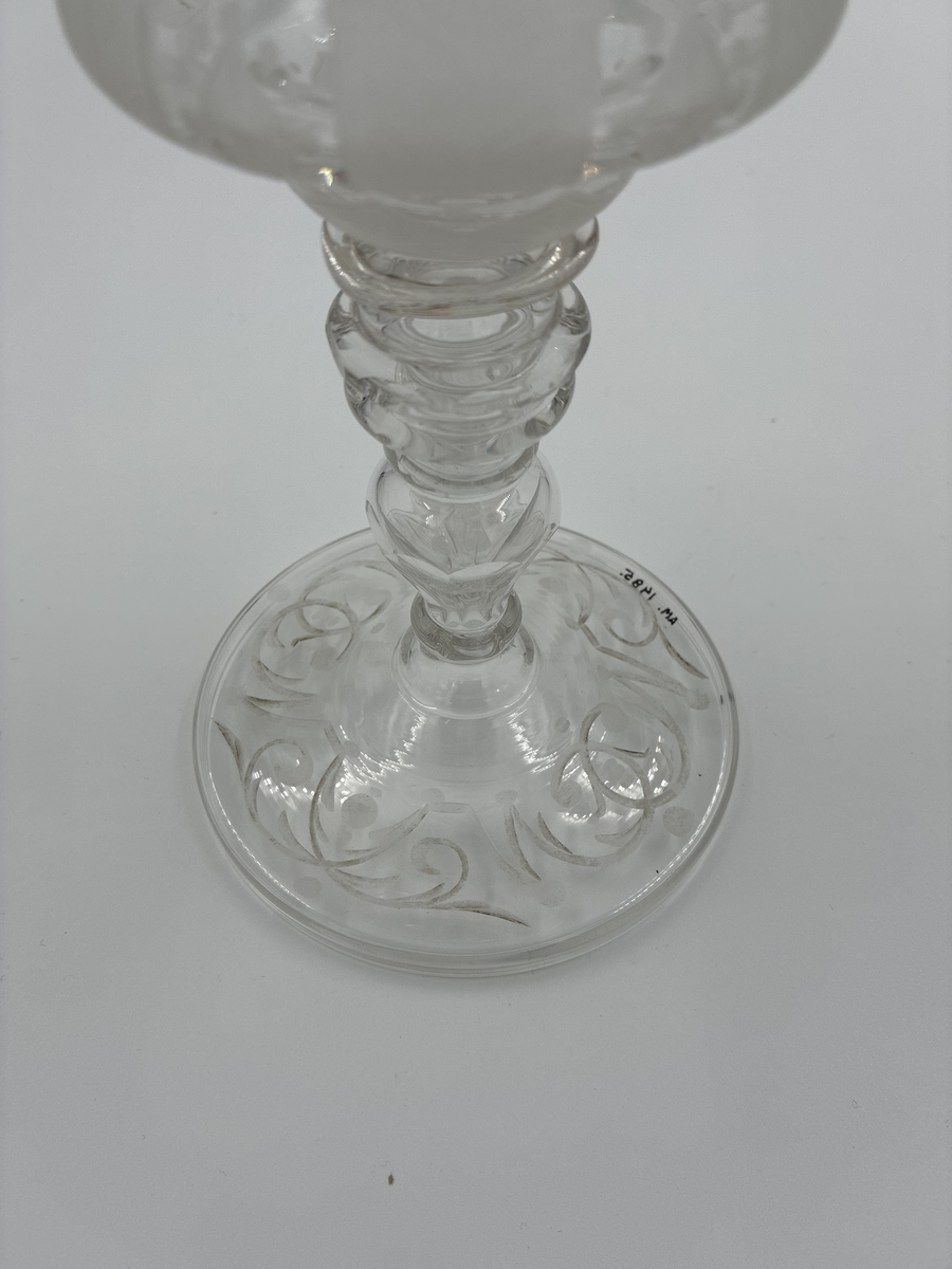 Pokal med lock. Av glas med riklig etsad dekor. 

Enligt säljarens uppgift har pokalen varit en gåva till fru von Proschwitz, Floda herrgård vid dennas 50-årsdag.
Efter hennes bortgång överlämnades pokalen som minnesgåva till dr G. Nystedt för dennas mångåriga tjänst som husläkare hos familjen Proschwitz.