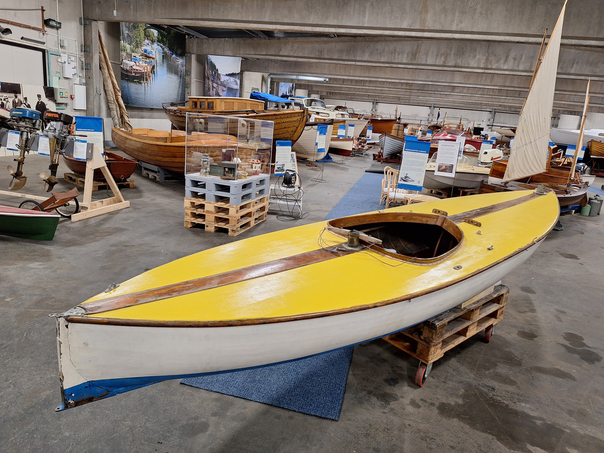 Segelkanot, klass III B, med Güntherrigg och centerbord. Fall, skot och block saknas. Byggd i mahogny, furu och duk. 
Vita fribord och gult däck. Mittfiskar och sarg i mahogny.