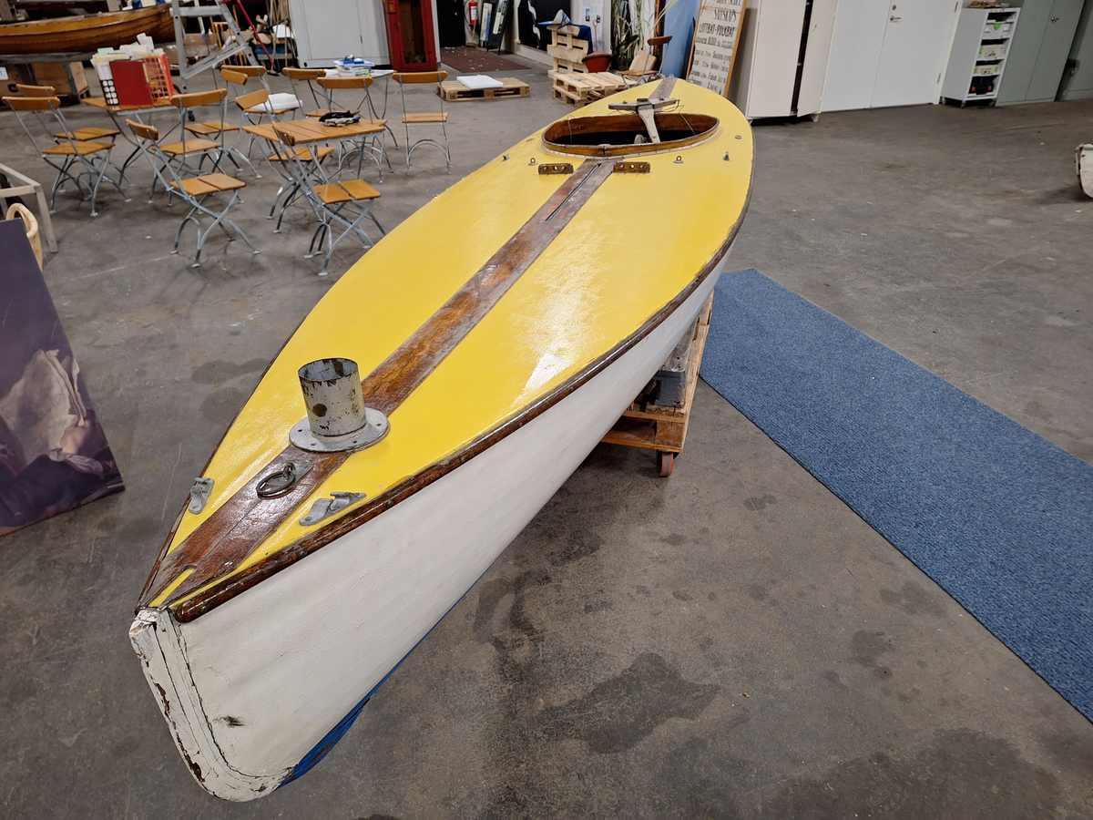 Segelkanot, klass III B, med Güntherrigg och centerbord. Fall, skot och block saknas. Byggd i mahogny, furu och duk. 
Vita fribord och gult däck. Mittfiskar och sarg i mahogny.