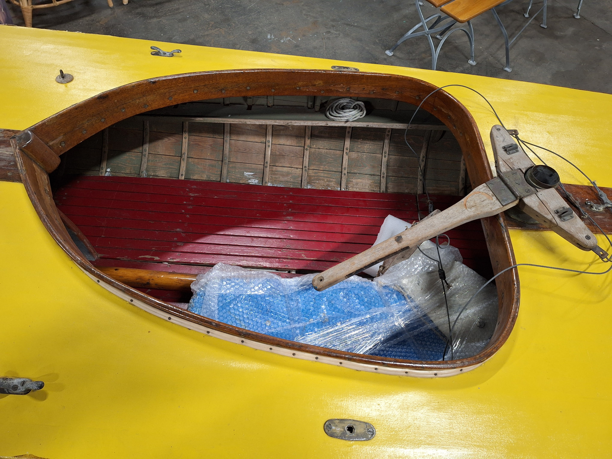 Segelkanot, klass III B, med Güntherrigg och centerbord. Fall, skot och block saknas. Byggd i mahogny, furu och duk. 
Vita fribord och gult däck. Mittfiskar och sarg i mahogny.