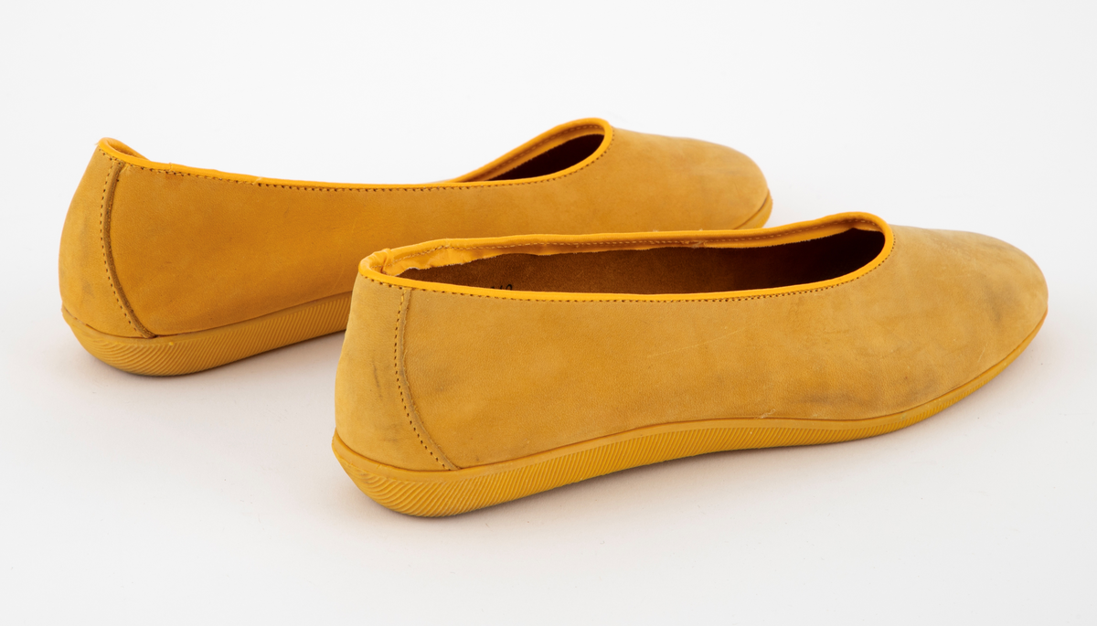 Ballerinasko med rundet tå i gult semsket skinn. Flat gummisåle med rifler. Ufôret. Den innvendig sålen er trukket med rødt stoff med hvite spetter. 
Høyre- og venstre sko har ulik størrelse.