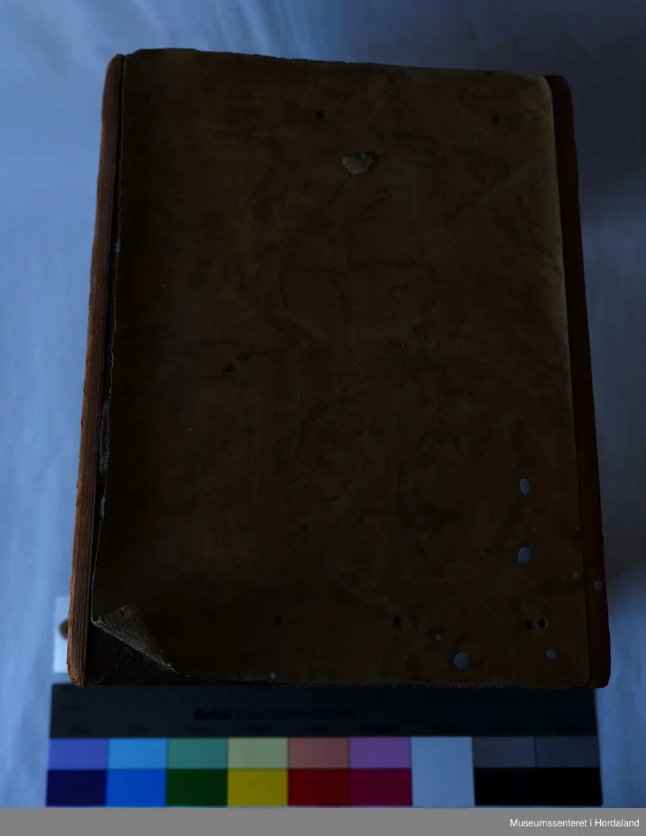 Liten, brun fotskammel av tre med linoleums-lignende lag på setet.