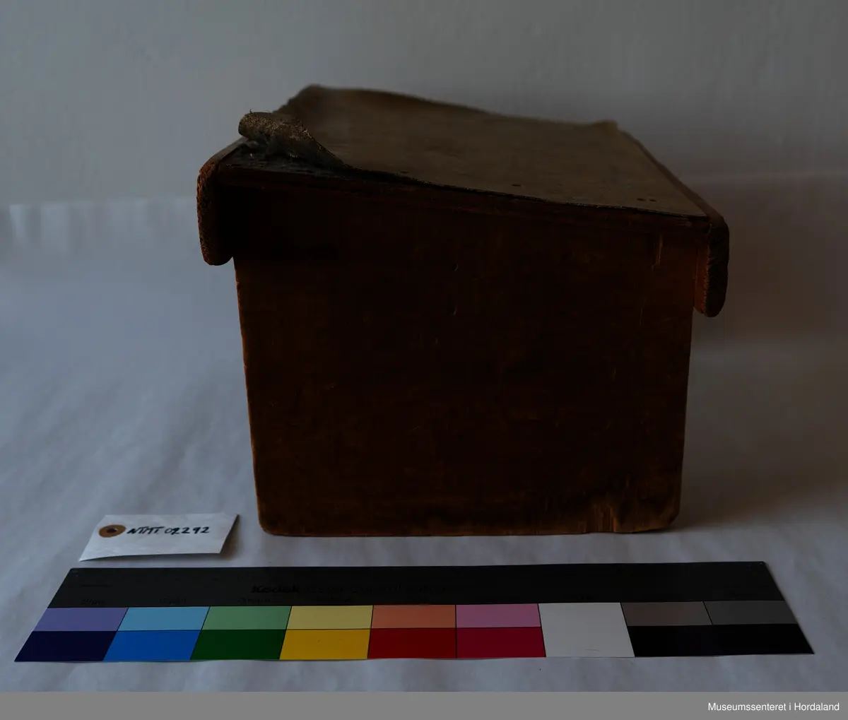 Liten, brun fotskammel av tre med linoleums-lignende lag på setet.