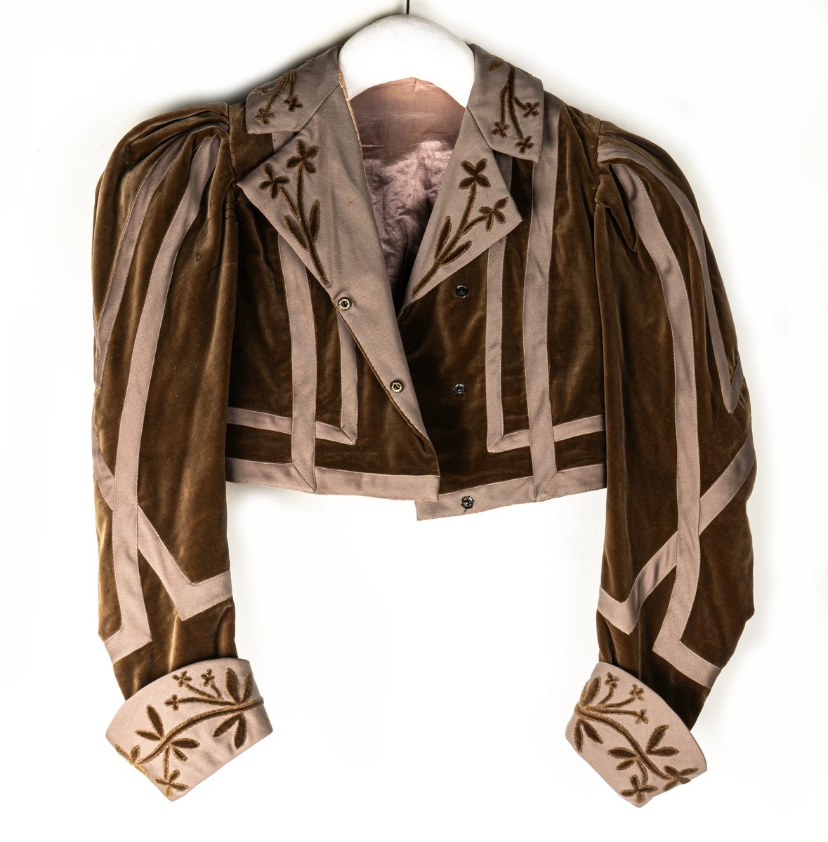 Del av dräkt/klänning.
b) Jacka, sammet. Krage och slag av gabardin med blommor av sammet. Knäppning fram. Långa puffärmar med slag. livet och ärmarna dekorerade med gabardinremsor. L fram 43cm, bak 37cm.