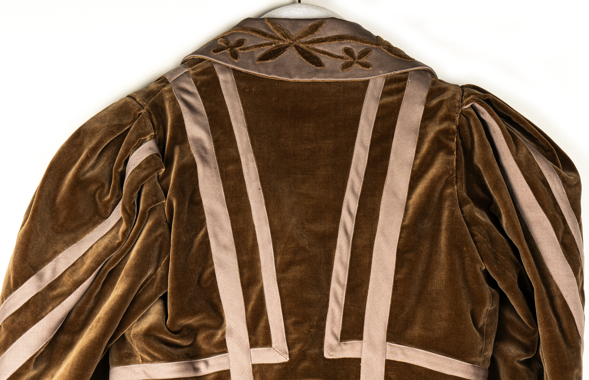 Del av dräkt/klänning.
b) Jacka, sammet. Krage och slag av gabardin med blommor av sammet. Knäppning fram. Långa puffärmar med slag. livet och ärmarna dekorerade med gabardinremsor. L fram 43cm, bak 37cm.