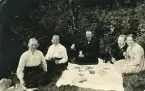 En grupp människor som har en picknick utomhus, troligen under tidigt 1900-tal. Text baksida kort: 