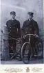 Två män i uniformsliknande kläder poserar med en tidig 