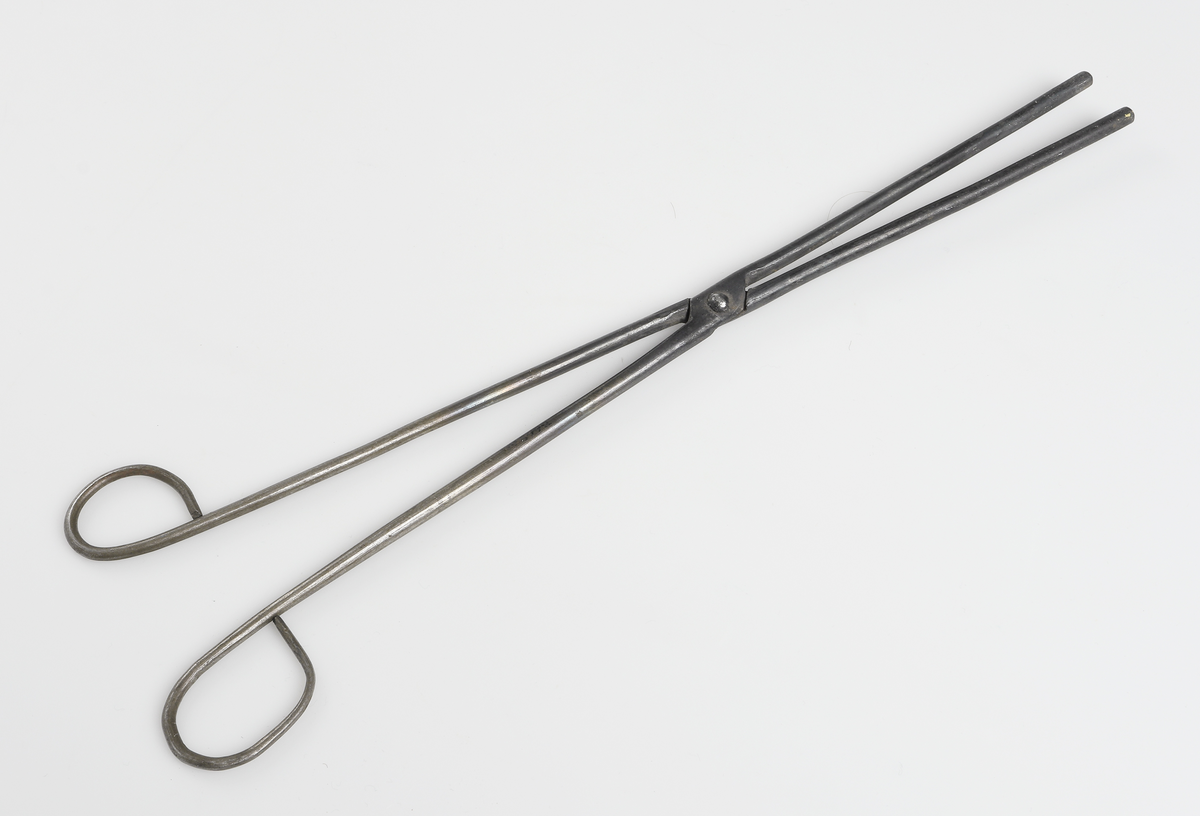 Piptång av metall med raka runda skänklar. Handtaget avslutas i fingeröglor. 
Användes exempelvis vid veckning av kragar, pipkragar, och skjortkrås mm. 

Inskrivet i huvudbok år 1936.