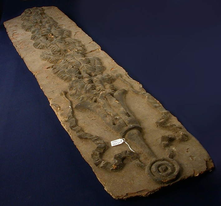 Modell till väggdekoration. Bladornament, i hög relief, upphängda med fladdrande band. (Massa, av trämassa med lin inblandat). Sönder i två delar.