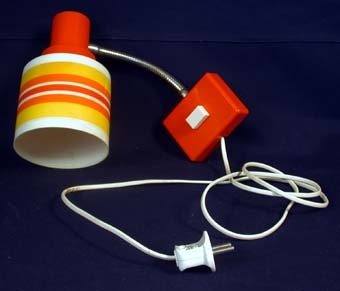 Lampfot/fundament i form av en rektangulär låda av orange och vit plast med borrade hål på baksidan så att man med hjälp av skruvar kan sätta upp den på väggen, samt en klisterlapp på vilken det står "VG 500-1. Max 40 W". På framsidan en fyrkantig knapp av vit plast, som fungerar som lampans strömbrytare när man vill tända och släcka lampan. Inuti sitter ena änden av en elektrisk sladd, i andra änden en stickkontakt som stoppas i ett elektriskt vägguttag. Från fundamentet går en arm i form av en grov, böjbar fjäder av metall. I toppen av armen en lamphållare där glödlampan skruvas fast, samt en lampskärm som sitter över glödlampan. På skärmen en fastklistrad dekorativ remsa med orange och gula ränder.